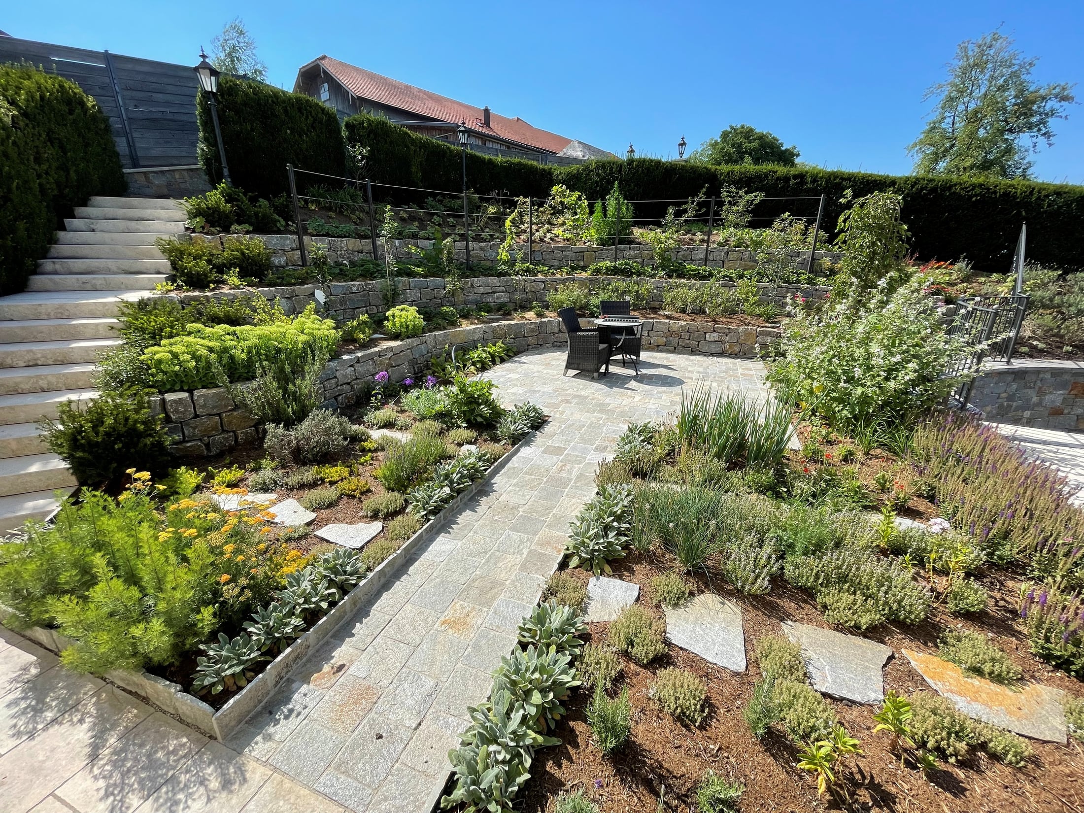 Terrassengarten mit bepflanzten Natursteinmauern und gepflastertem Sitzplatz